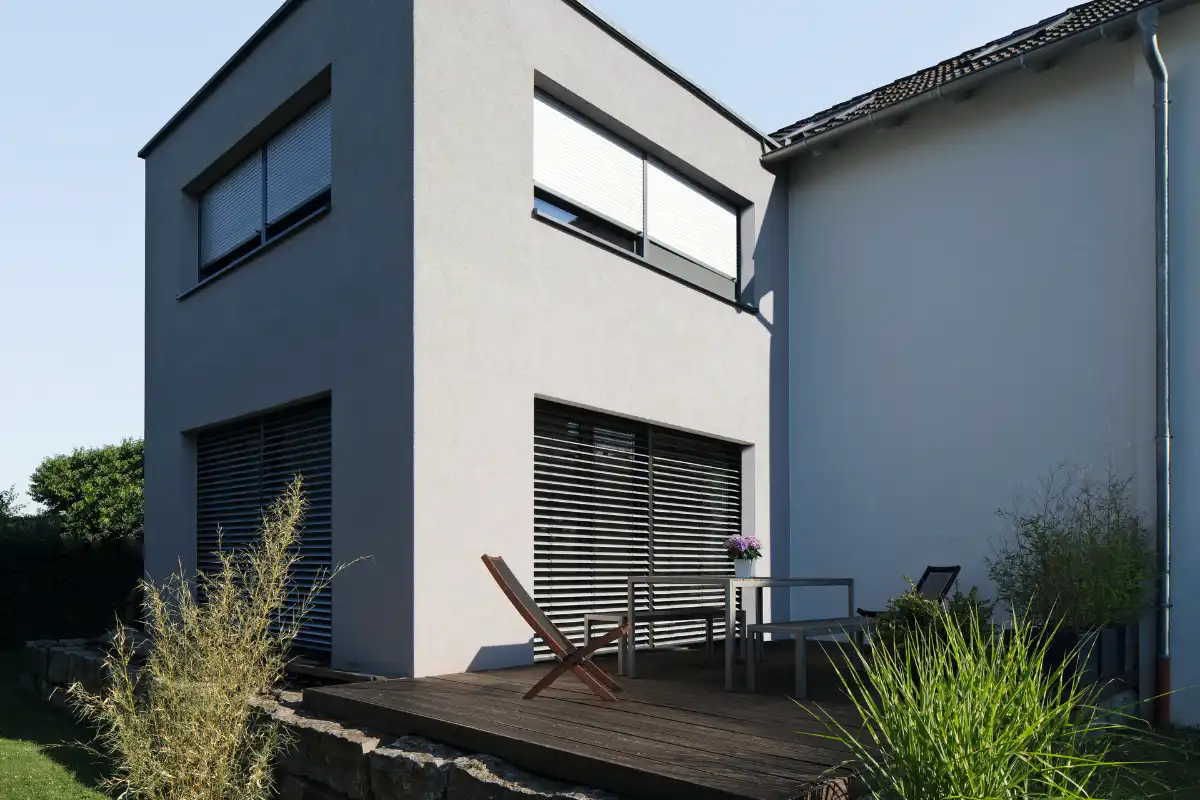 Haus mit Rolläden an den Fenstern und einer Terrasse Moderne Wohnhausfassade mit Terrasse und Garten