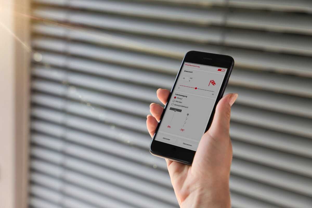 Smartphone mit Steuerungsapp für Jalousien vor Fenster